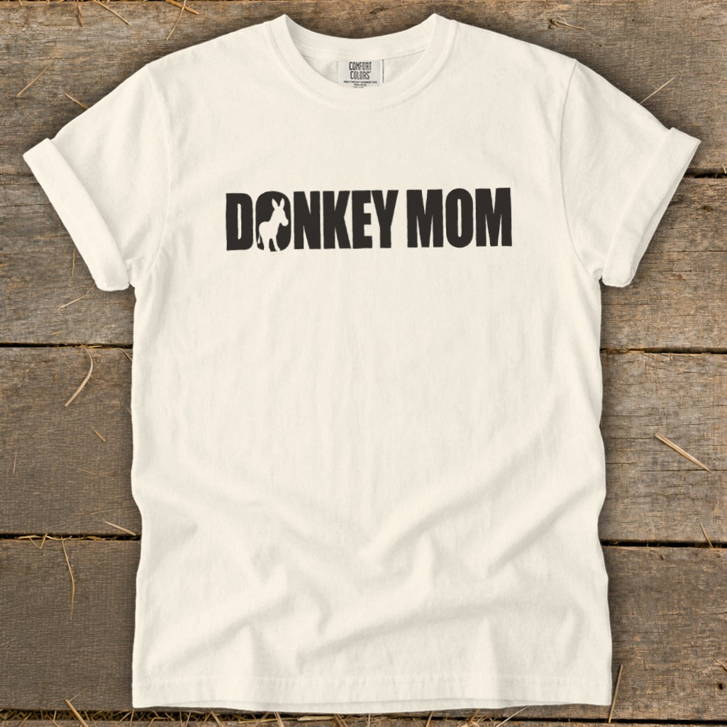 A cream-colored short-sleeved t-shirt with black text reading DONKEY MOM, featuring a donkey silhouette inside the letter O.