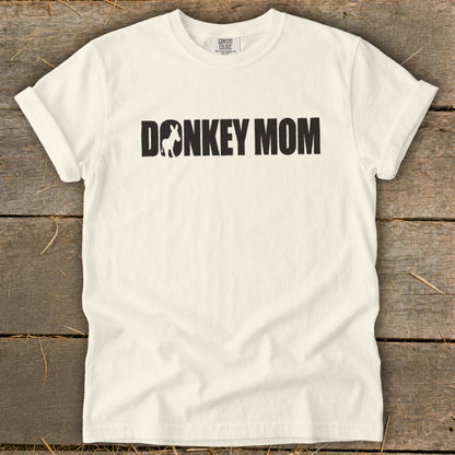 A cream-colored short-sleeved t-shirt with black text reading DONKEY MOM, featuring a donkey silhouette inside the letter O.