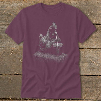 T-shirt graphic of a chicken drinking from a cup on hay.