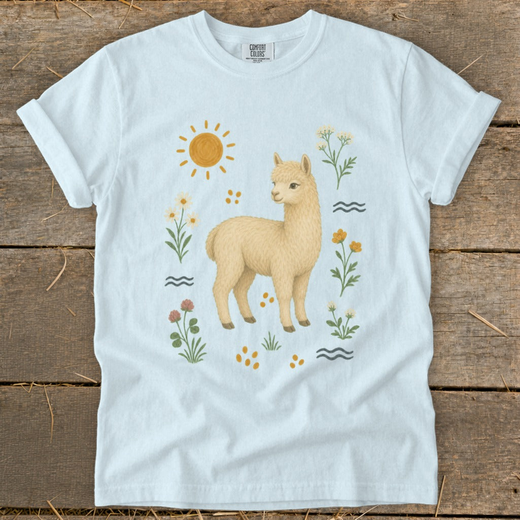 Light blue t-shirt with an illustrated llama surrounded by flowers, sun, and waves.