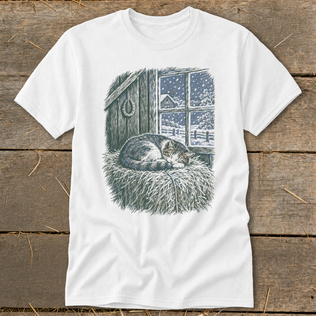 White t-shirt with a drawing of a cat sleeping on hay by a snowy window.