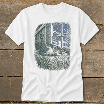 White t-shirt with a drawing of a cat sleeping on hay by a snowy window.