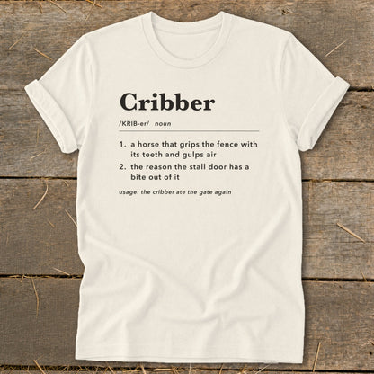 A cream-colored t-shirt with a humorous dictionary definition of the word cribber printed on the front.