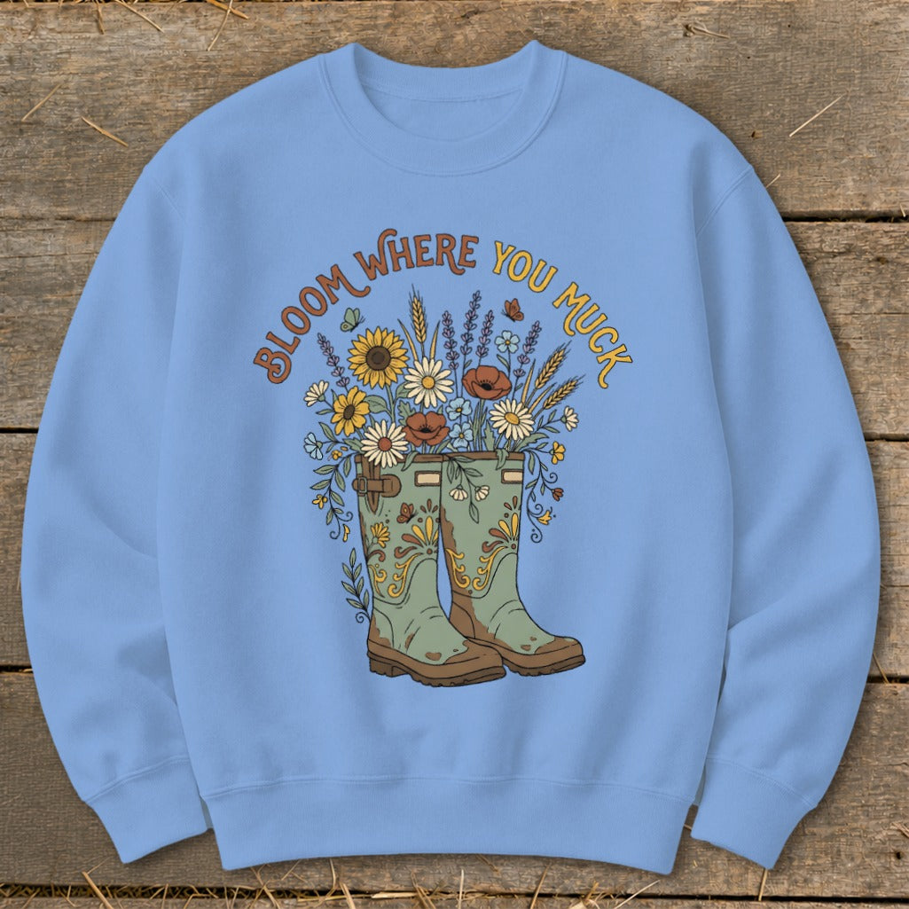Light blue sweatshirt with "Bloom Where You Muck" text and floral garden boot graphic.