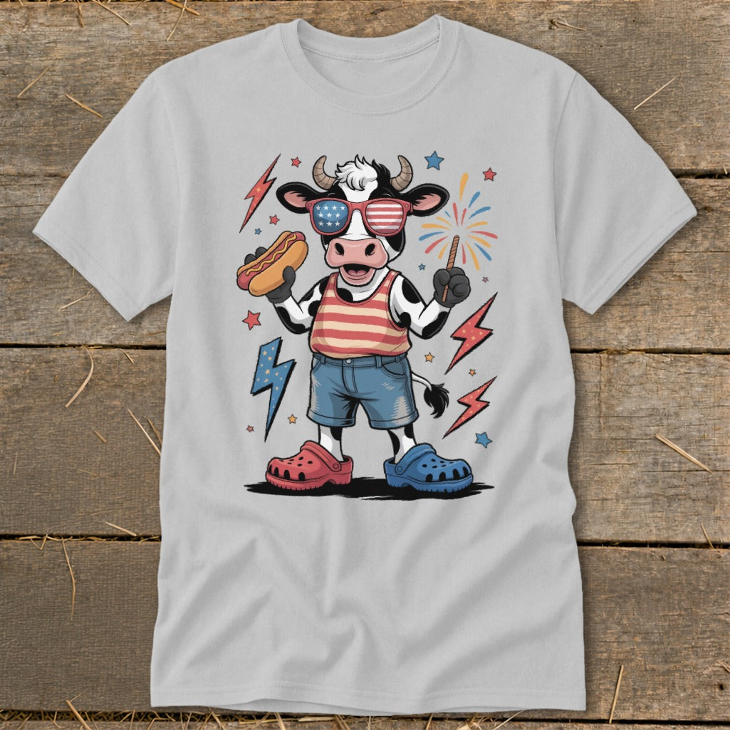 Cartoon cow wearing patriotic sunglasses holds a hot dog and a sparkler.