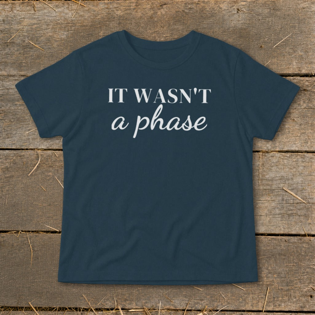Navy t-shirt with white text "IT WASN'T a phase" on wooden surface.