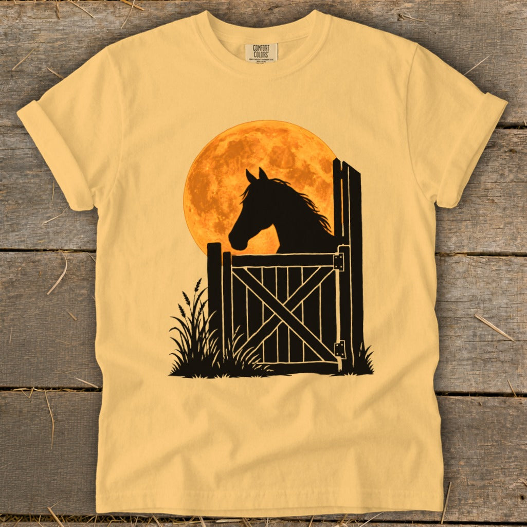 Yellow t-shirt featuring a black silhouette graphic of a horse peering over a wooden gate against a large orange moon.