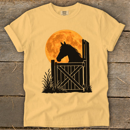 Yellow t-shirt featuring a black silhouette graphic of a horse peering over a wooden gate against a large orange moon.