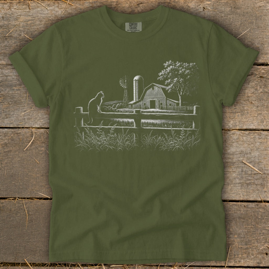 Green t-shirt with white line drawing of a cat on a fence, barn, windmill, and tree.