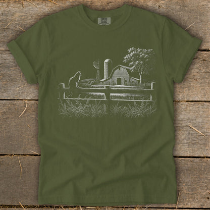 Green t-shirt with white line drawing of a cat on a fence, barn, windmill, and tree.