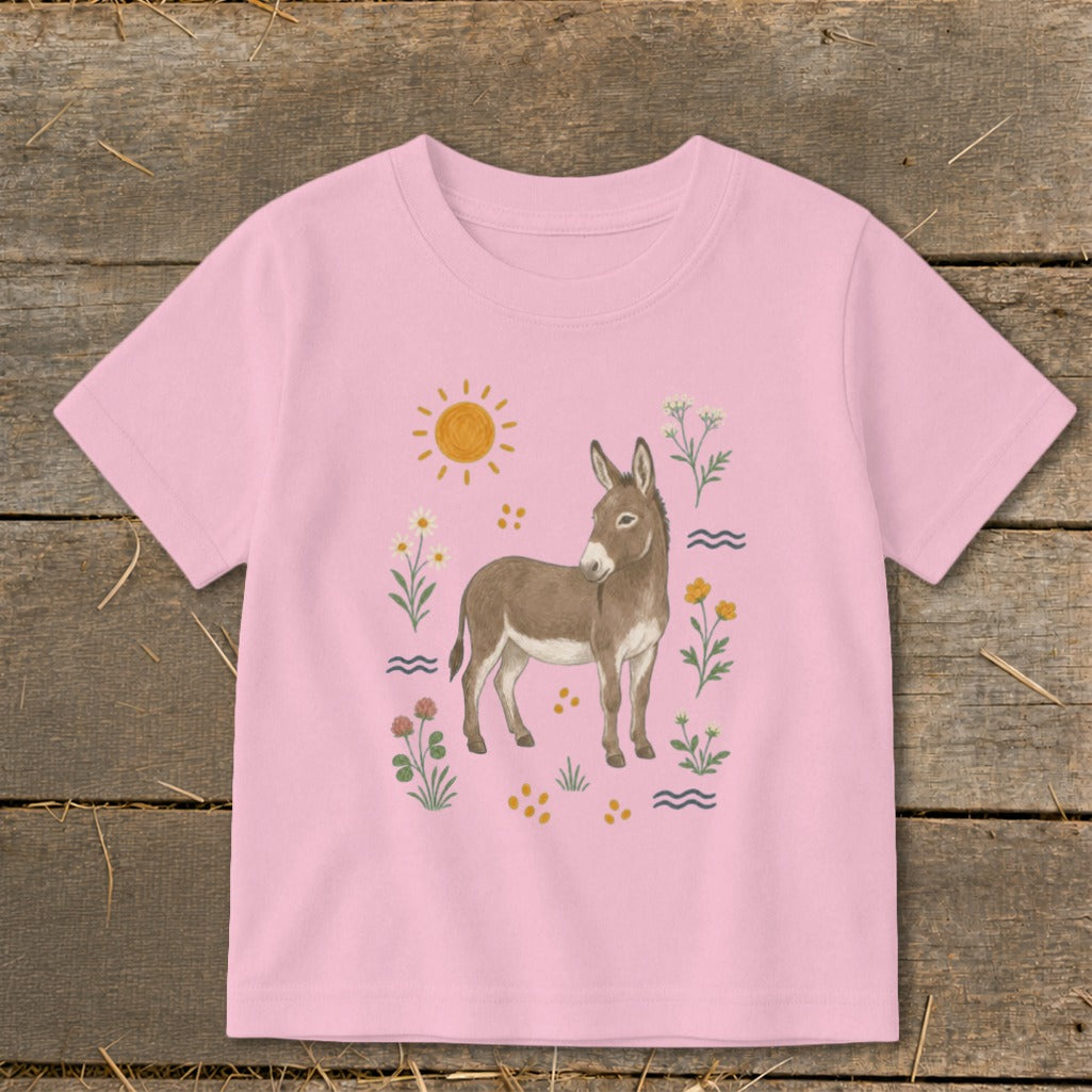 Pink t-shirt with a watercolor illustration of a donkey surrounded by flowers and a sun.
