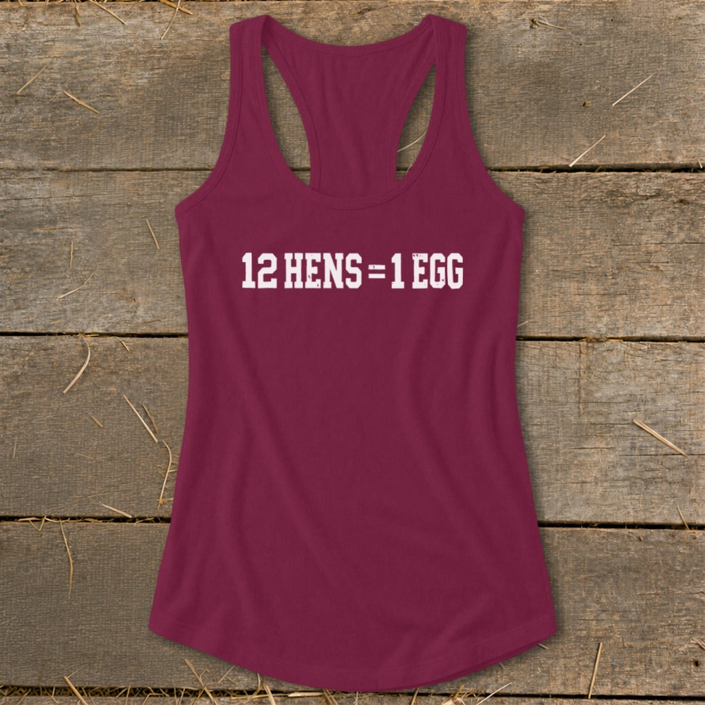 Maroon women's racerback tank top featuring the white text 12 HENS = 1 EGG, laid flat on a rustic wooden surface.