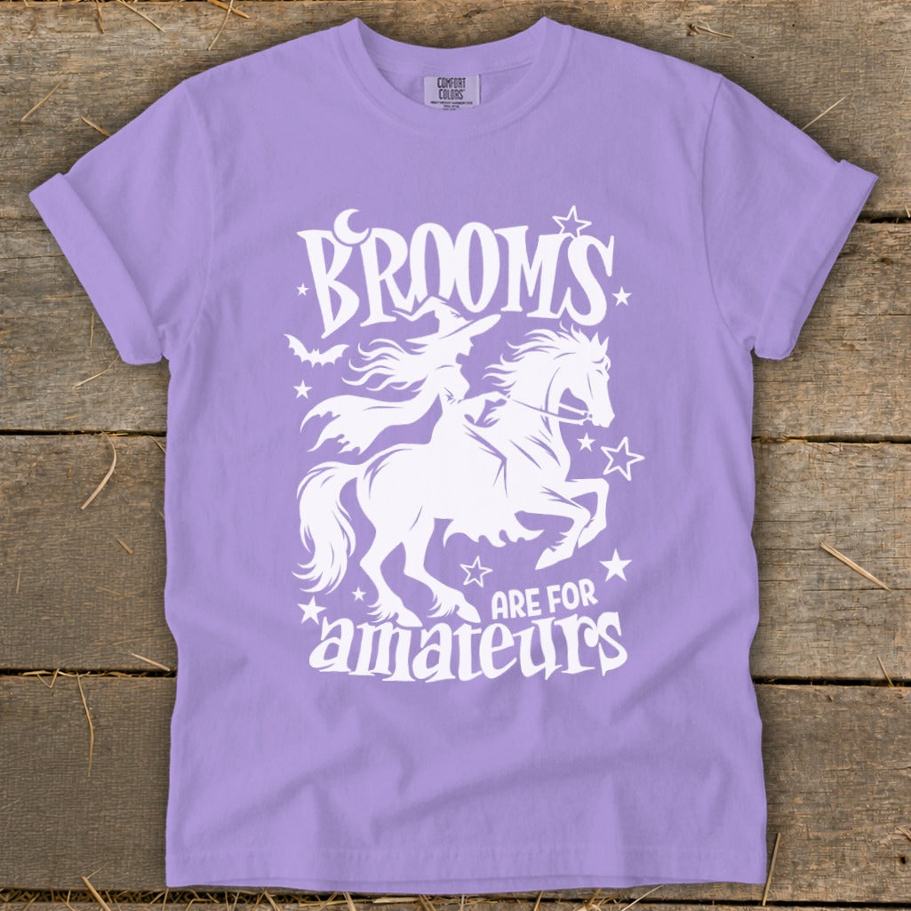 Purple t-shirt with white graphic of a witch on a horse and text "Brooms are for amateurs."