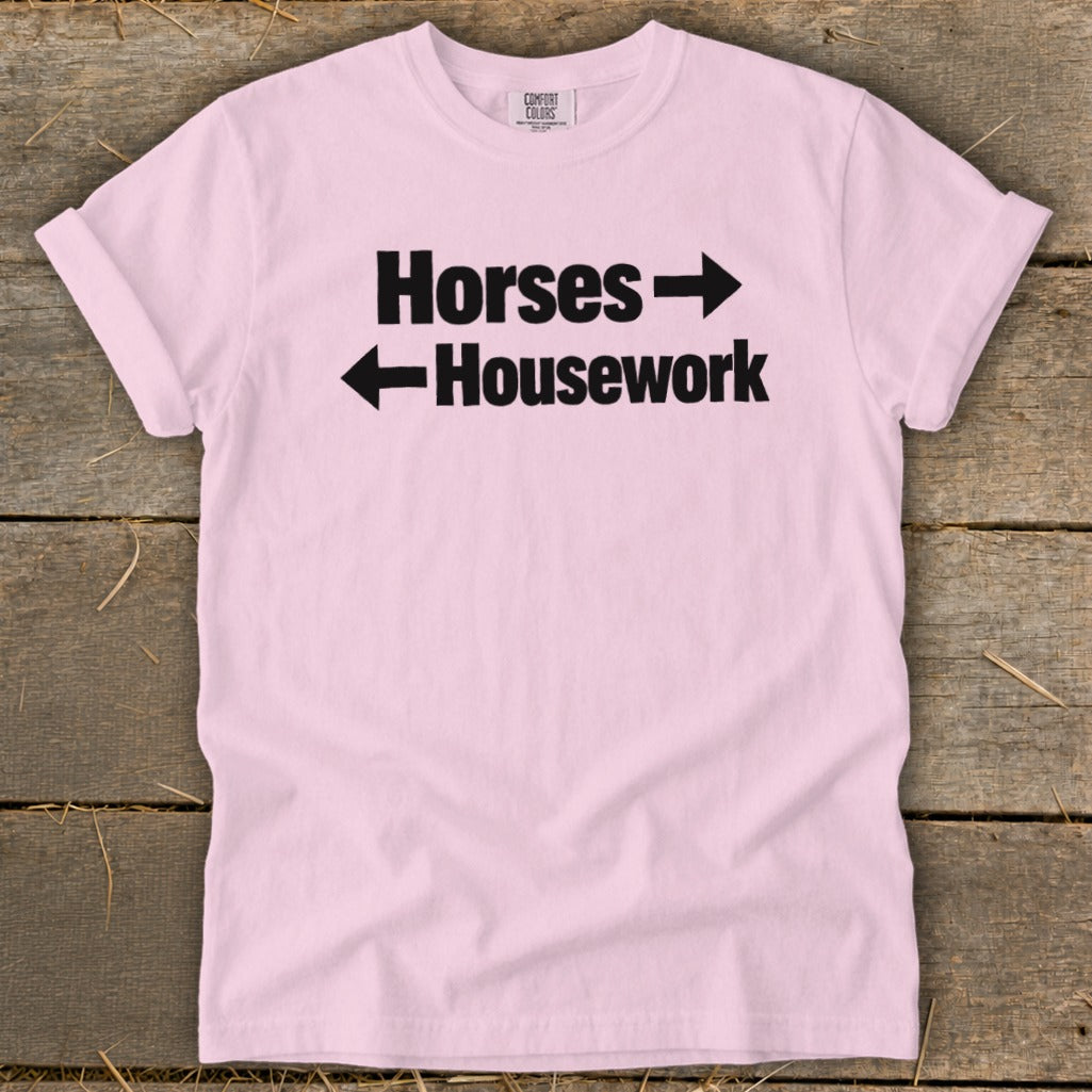A light pink t-shirt with rolled sleeves features black text reading Horses with a right-pointing arrow above Housework with a left-pointing arrow.