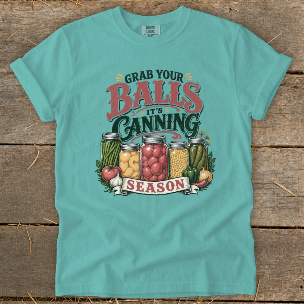 T-shirt with "Grab your balls, it's canning season" graphic and jars of produce.