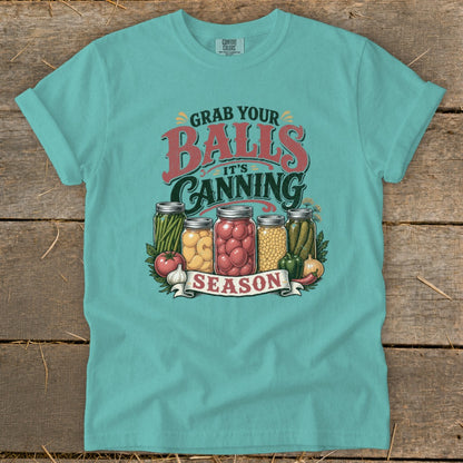 T-shirt with "Grab your balls, it's canning season" graphic and jars of produce.