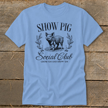Light blue t-shirt with "SHOW PIG Social Club GROW 'EM AND SHOW 'EM" text and a pig graphic.