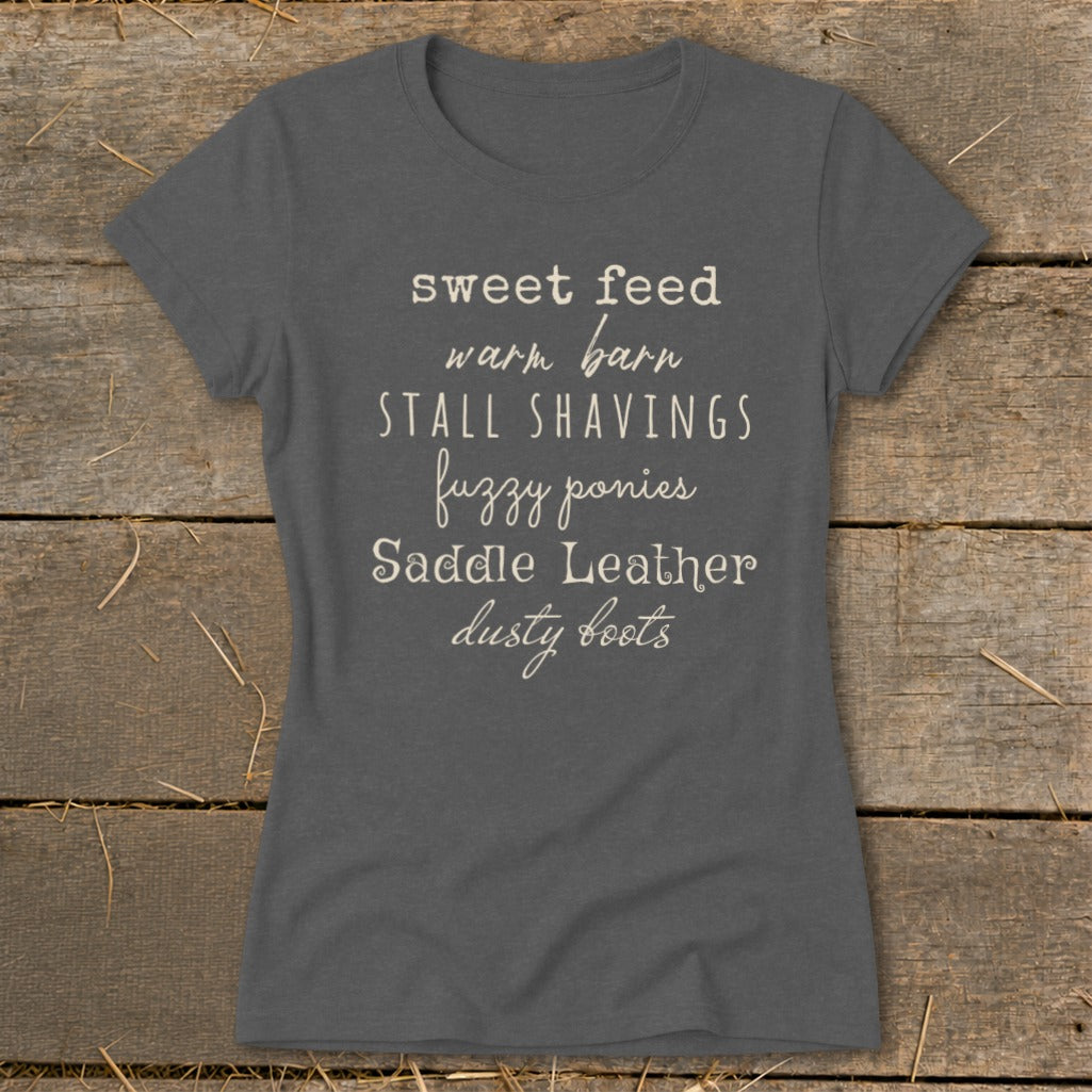 Dark gray t-shirt with text: sweet feed, warm barn, stall shavings, fuzzy ponies, saddle leather, dusty boots.