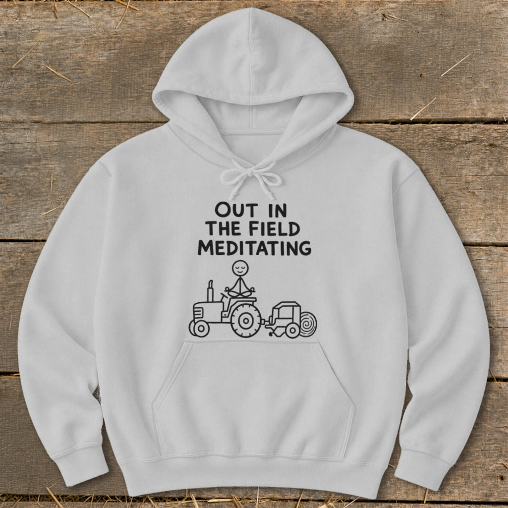 White hoodie with text "OUT IN THE FIELD MEDITATING" and stick figure meditating on a tractor.