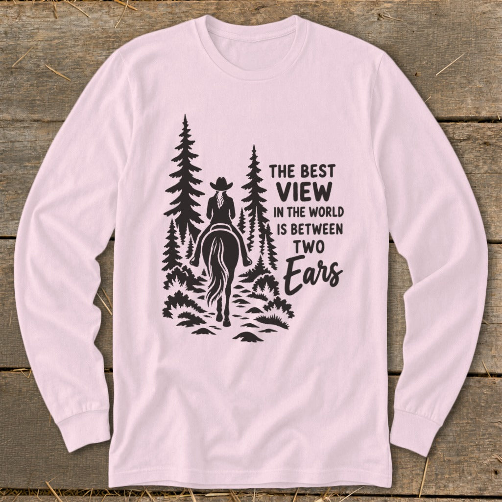 Light pink long-sleeve shirt featuring a black graphic of a horseback rider in the woods with text reading The best view in the world is between two ears.