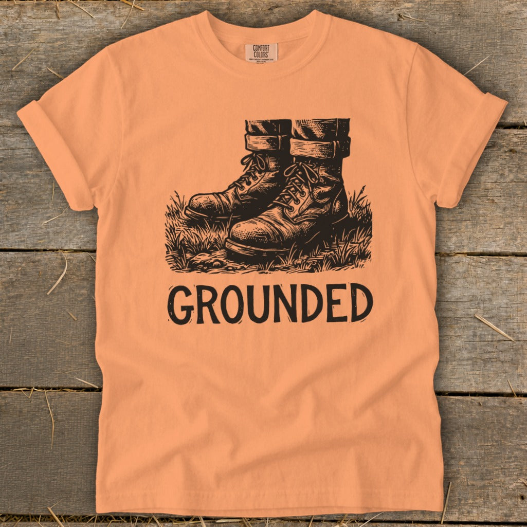Peach t-shirt with black graphic of boots and text "GROUNDED."