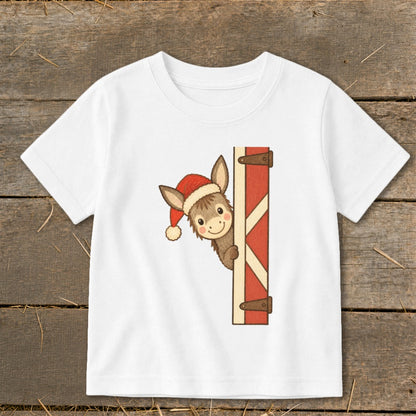 White t-shirt with cartoon donkey wearing Santa hat peeking from behind barn door.