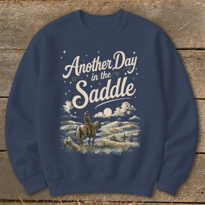 Crewneck sweatshirt with "Another Day in the Saddle" text and cowboy on horseback graphic.