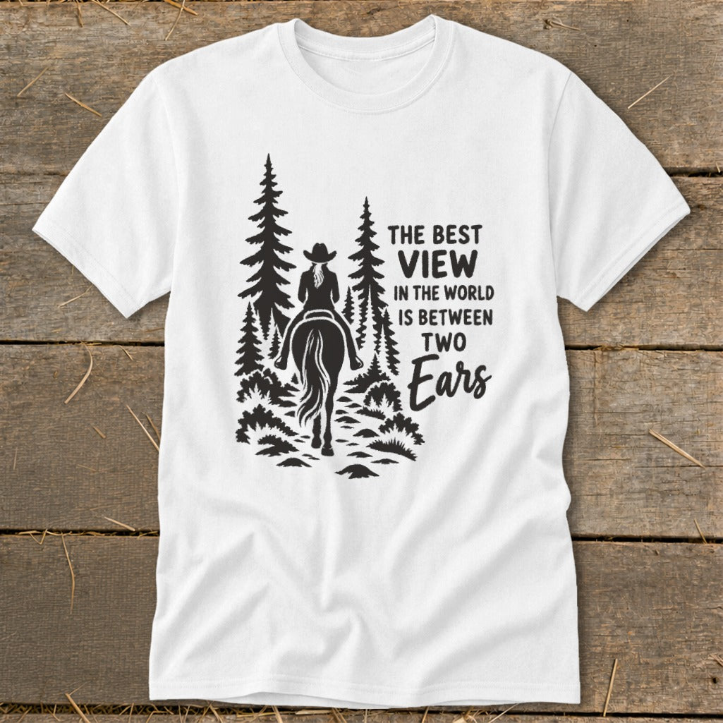 White t-shirt featuring a black graphic of a horseback rider in the forest with text that reads, "The best view in the world is between two ears."