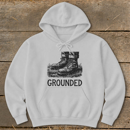 White hoodie with a black graphic of boots in grass and the word "GROUNDED".