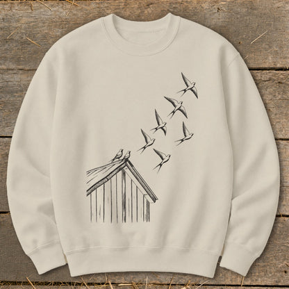 Beige crewneck sweatshirt featuring a black ink illustration of birds taking flight from a cabin roof.