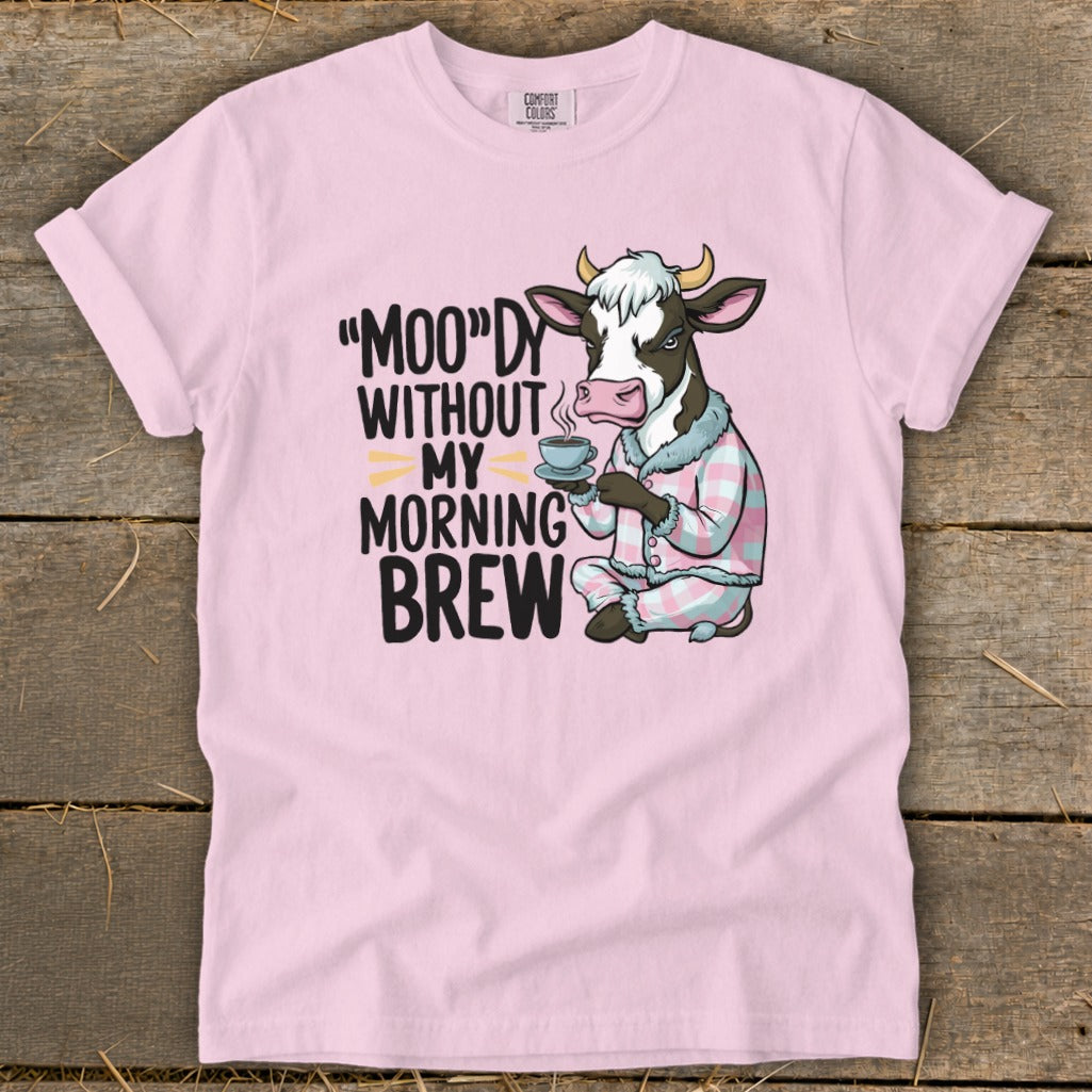 Pink t-shirt with a cartoon cow in pajamas holding a coffee cup and text "Moo"dy Without My Morning Brew."