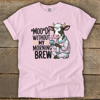 Pink t-shirt with a cartoon cow in pajamas holding a coffee cup and text "Moo"dy Without My Morning Brew."