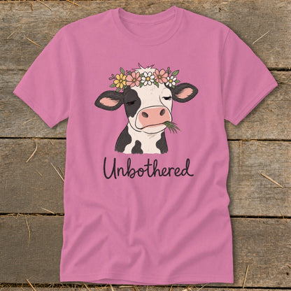 Pink t-shirt with a drawing of a cow wearing a flower crown, chewing grass, with text "Unbothered".