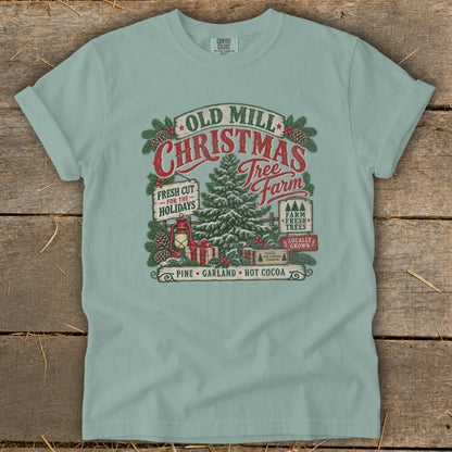 T-shirt with Old Mill Christmas Tree Farm graphic featuring pine trees, gifts, and lantern.