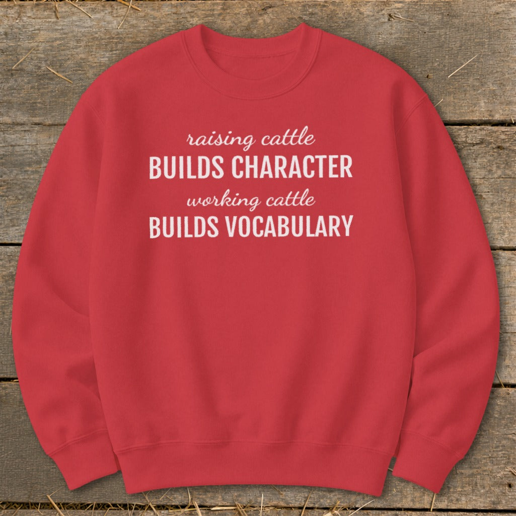 Red crewneck sweatshirt with white text reading "raising cattle BUILDS CHARACTER working cattle BUILDS VOCABULARY."