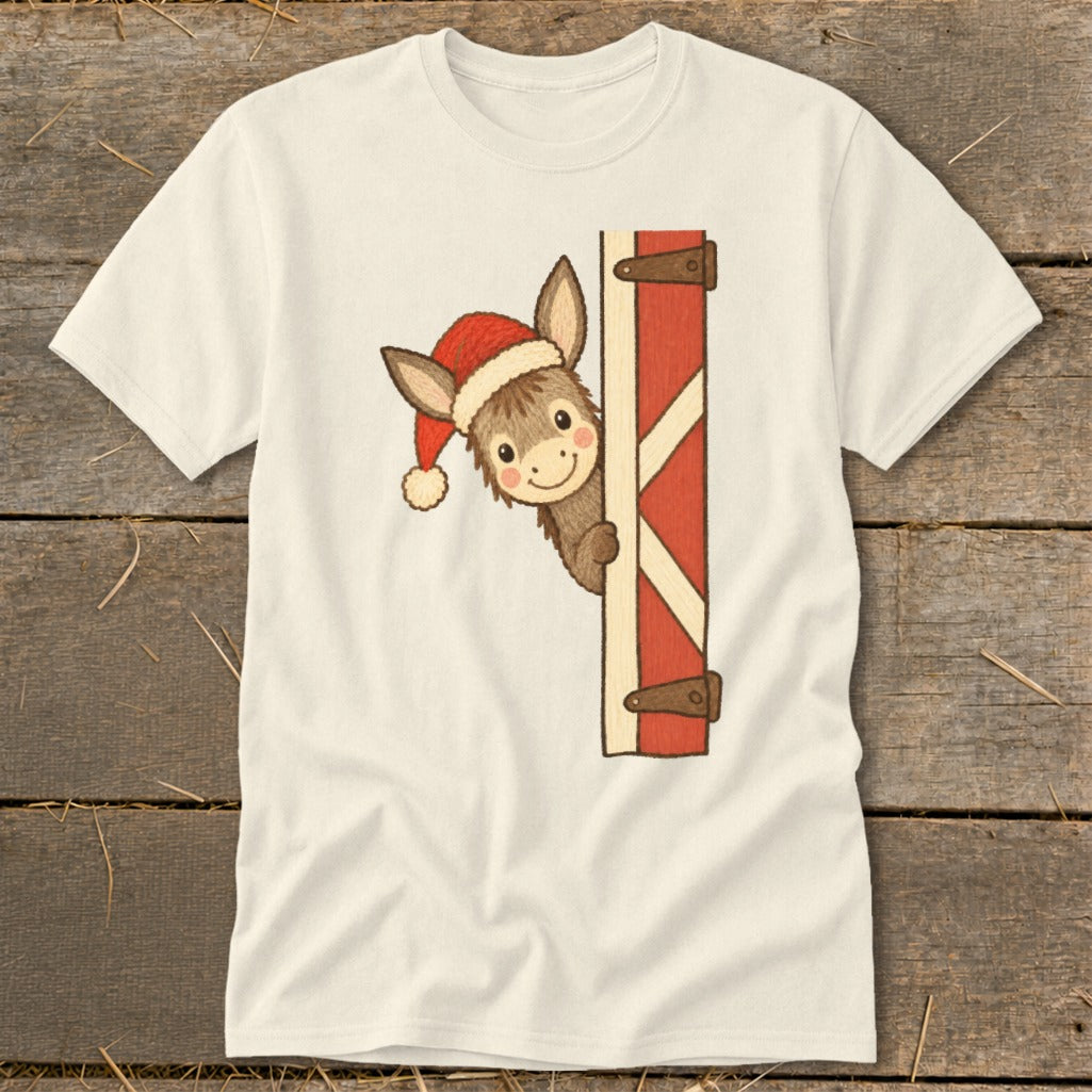 Donkey wearing Santa hat peeking from behind red barn door on cream t-shirt.