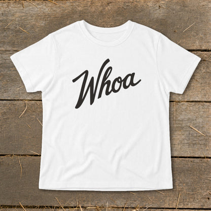 White t-shirt with "Whoa" in black script text on wooden background.