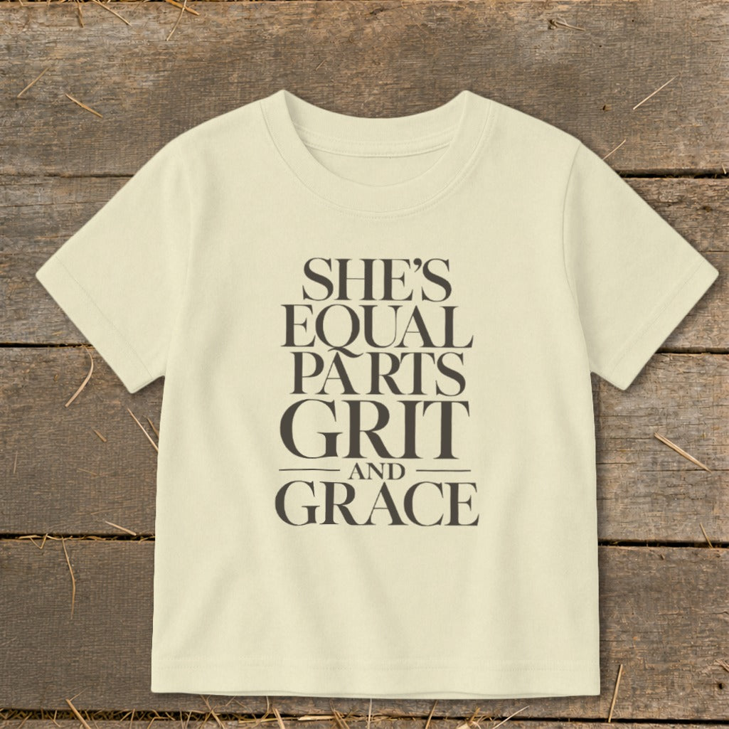 Light yellow t-shirt with dark gray text that reads "SHE'S EQUAL PARTS GRIT AND GRACE".