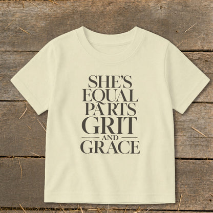 Light yellow t-shirt with dark gray text that reads "SHE'S EQUAL PARTS GRIT AND GRACE".