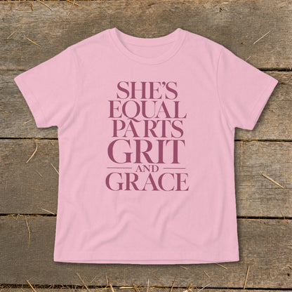 Pink t-shirt with text "SHE'S EQUAL PARTS GRIT AND GRACE" in deep purple.