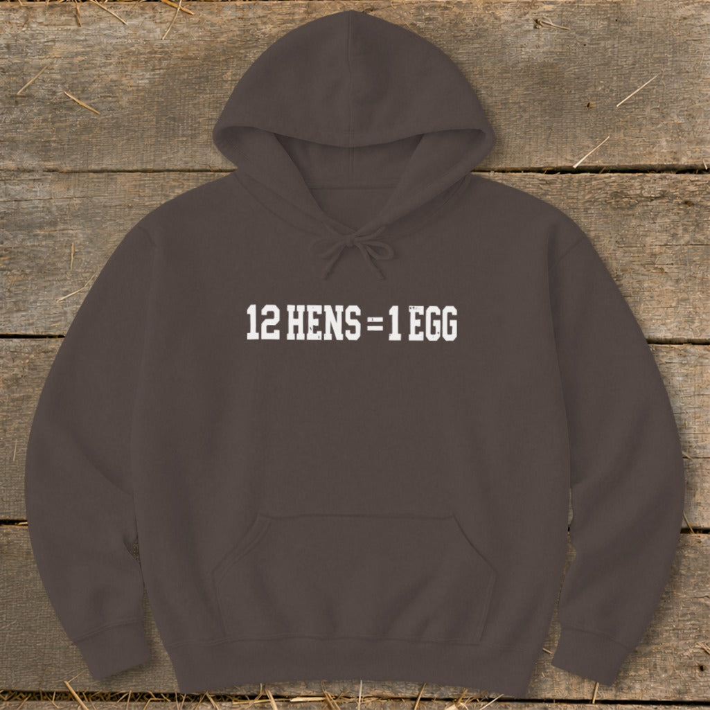 Dark brown hooded sweatshirt with white text on the chest reading 12 HENS = 1 EGG, laid flat on a rustic wooden background.