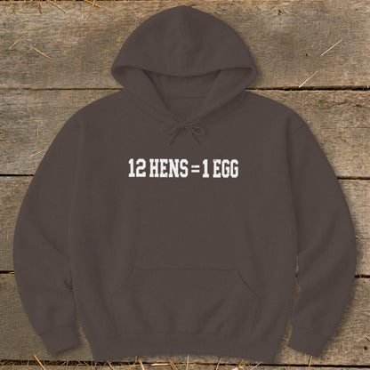 Dark brown hooded sweatshirt with white text on the chest reading 12 HENS = 1 EGG, laid flat on a rustic wooden background.