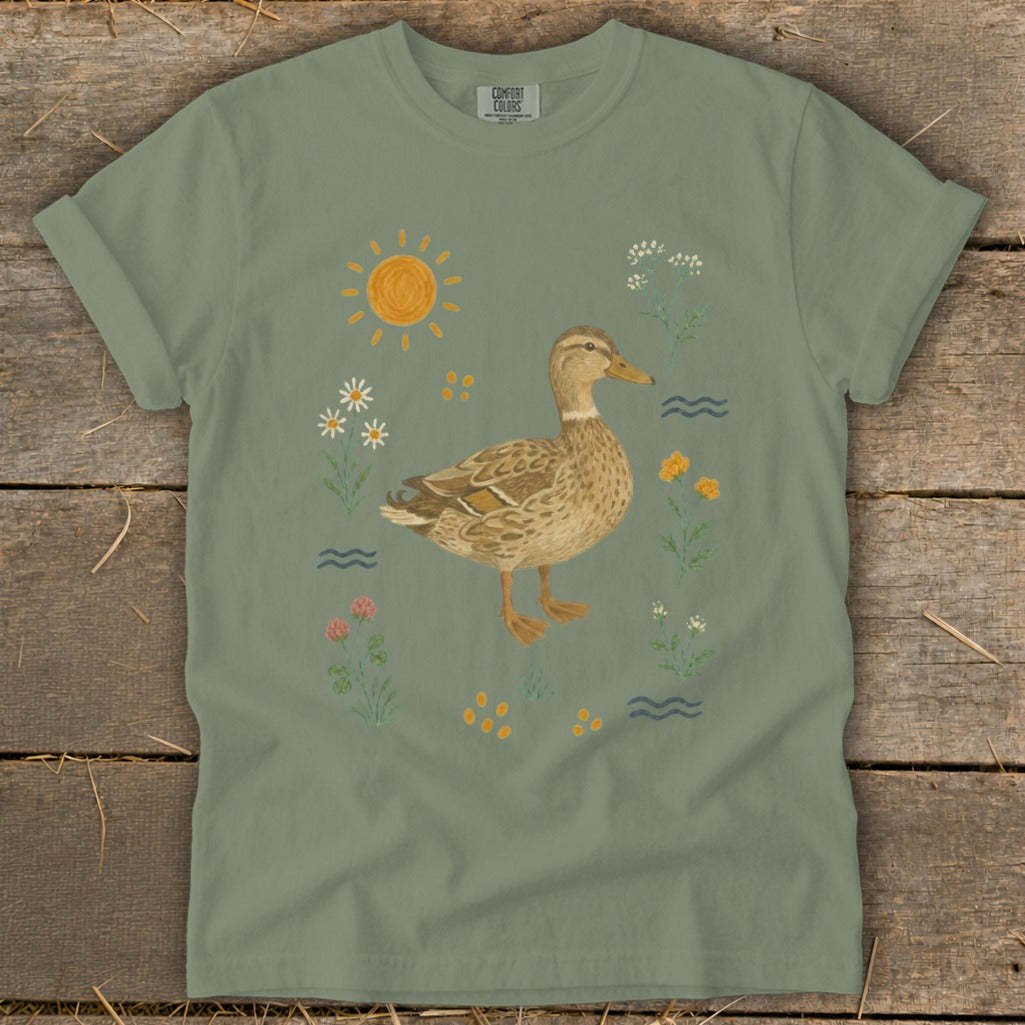 T-shirt graphic with a mallard duck surrounded by wildflowers, sun, and water.
