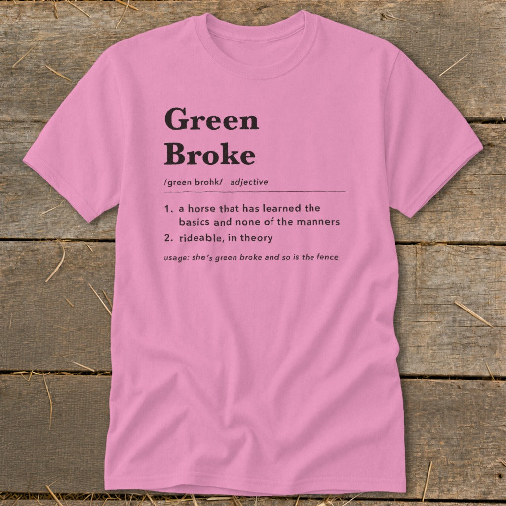Pink t-shirt with black text featuring a humorous dictionary definition of Green Broke on a wooden surface.