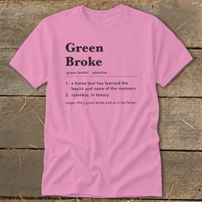 Pink t-shirt with black text featuring a humorous dictionary definition of Green Broke on a wooden surface.