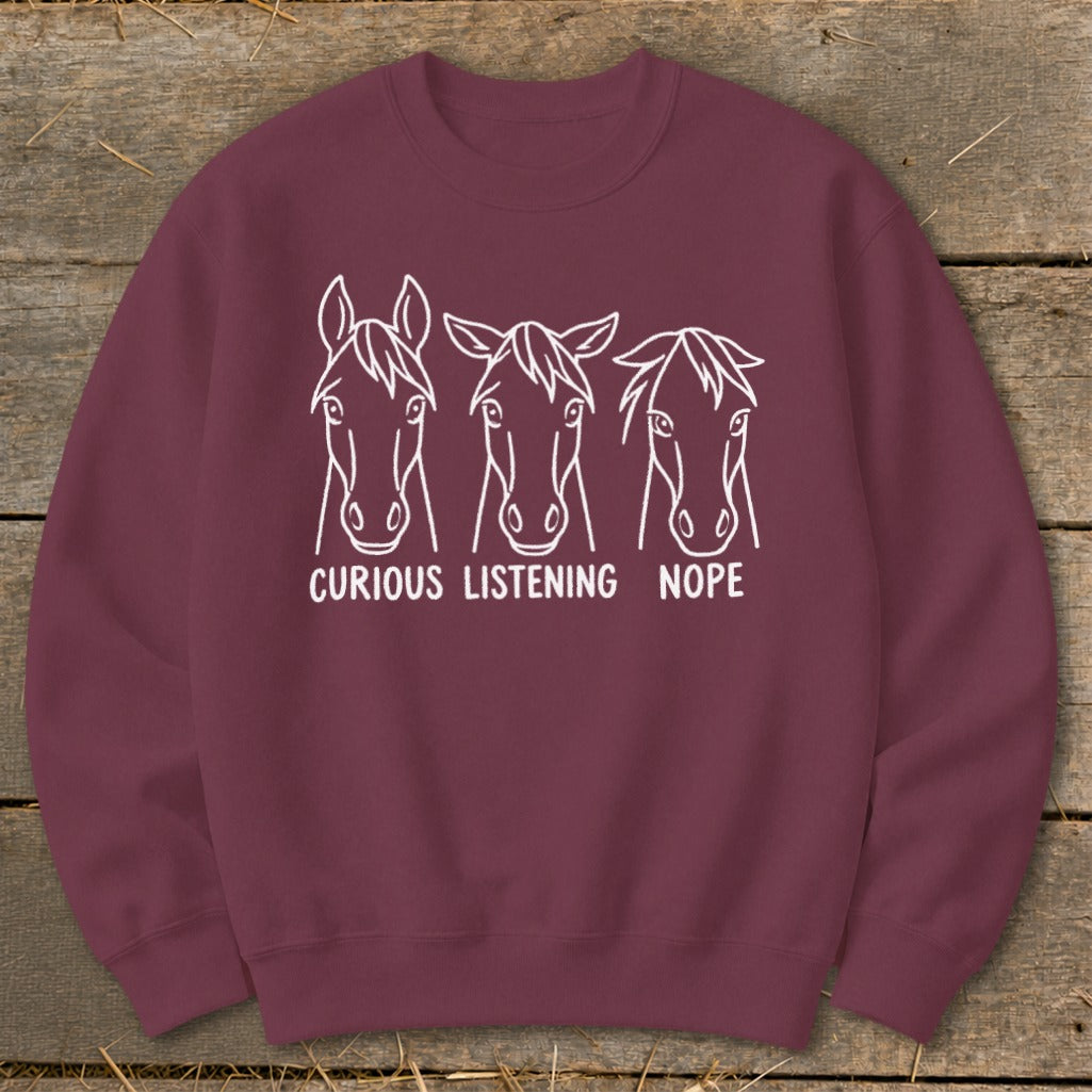 Maroon crewneck sweatshirt featuring white line art of three horse heads with the text "CURIOUS," "LISTENING," and "NOPE."