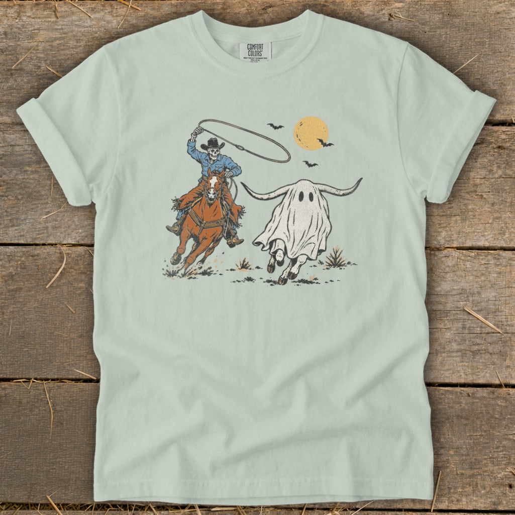 Skeleton cowboy on horseback lassoes a running ghost with horns under a yellow moon.