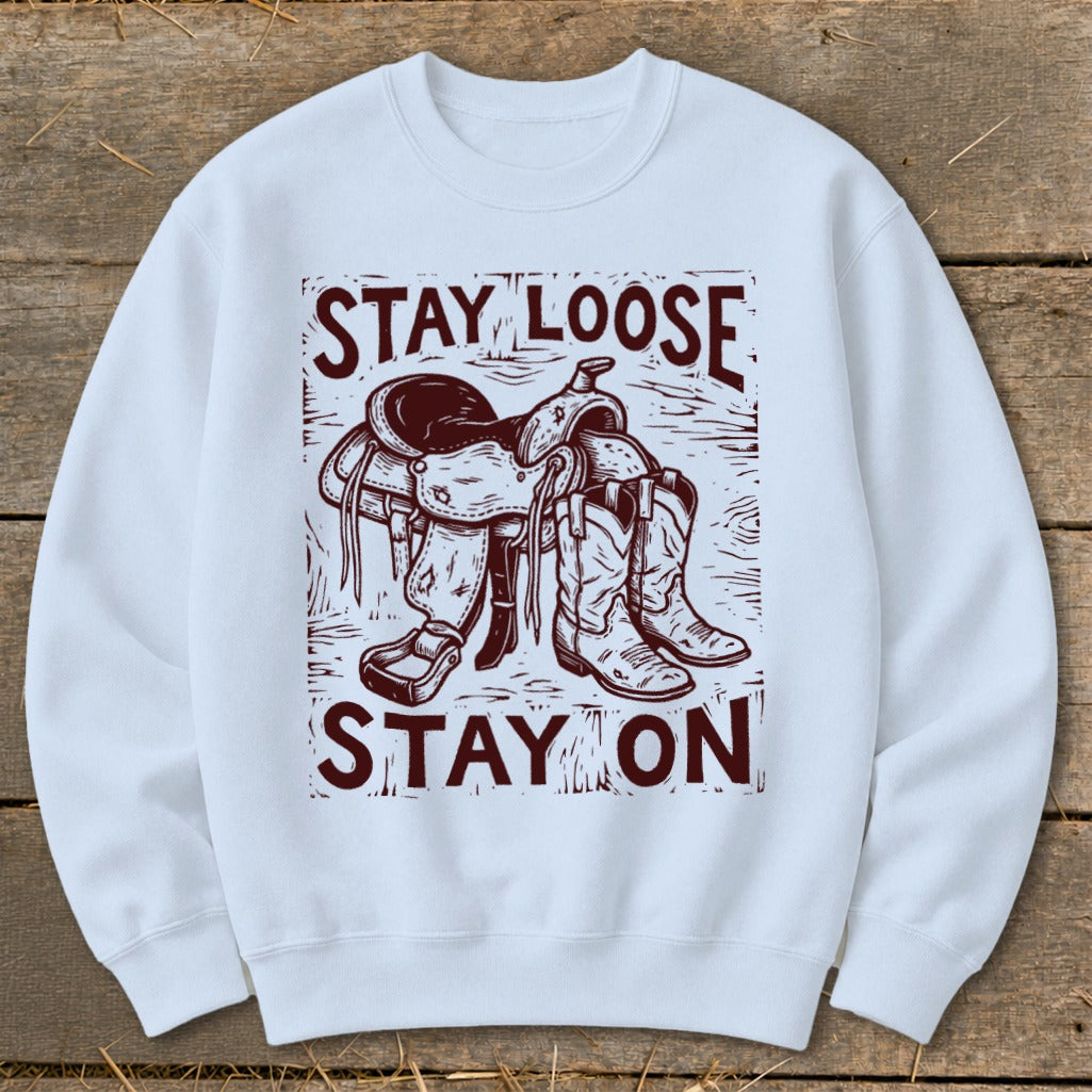 White sweatshirt with a graphic of a saddle and boots reading "STAY LOOSE STAY ON."