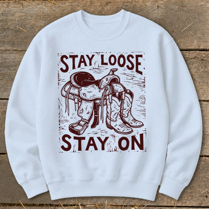 White sweatshirt with a graphic of a saddle and boots reading "STAY LOOSE STAY ON."
