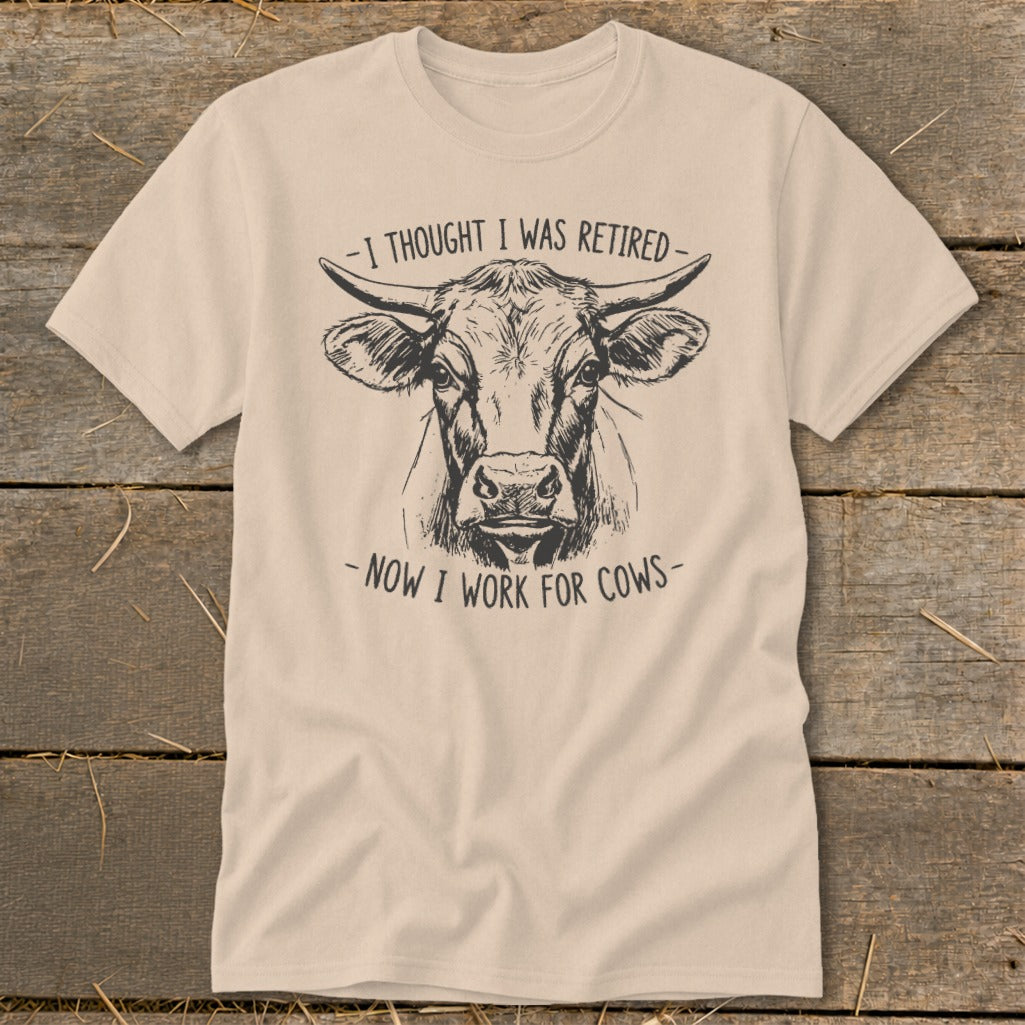 Light tan t-shirt with a sketch of a cow's head and text reading "I thought I was retired - now I work for cows."